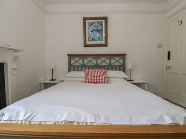 A bedroom with a bed with white sheets and a red checkered pillow two bedside tables with lamps a framed picture on the wall and a door on the right at Lookout in Mousehole