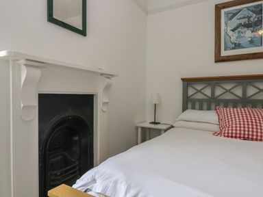 A bedroom with a bed red check pillow side table lamp fireplace and wall art at Lookout in Mousehole