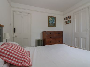 A bedroom with a bed with checkered pillow a wooden chest of drawers and framed pictures on the wall at Lookout in Mousehole
