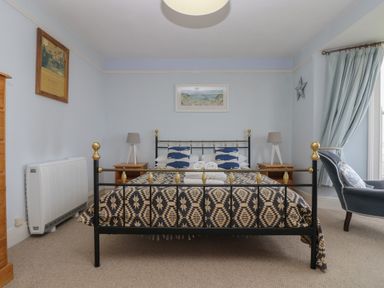 A bedroom with a metal bed frame two bedside tables with lamps a chair and window with curtains at Lookout in Mousehole