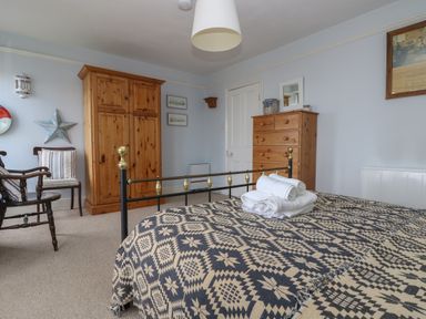 A bedroom with a patterned bedspread on a bed and wooden wardrobes and chairs at Lookout in Mousehole