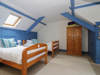 A bedroom with two single wooden beds blue beams on the ceiling a wooden wardrobe and a skylight window at Lookout in Mousehole