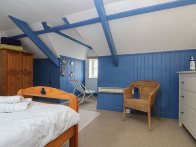 A bedroom with blue painted wood paneling and beams a wooden bed a wicker chair a white chest of drawers and a wooden wardrobe at Lookout in Mousehole