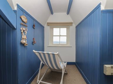 A small room with blue paneled walls a window at the end and a striped deck chair at Lookout in Mousehole