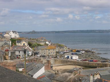 A coastal village with houses near a harbor and parked cars by the sea at Lookout in Mousehole