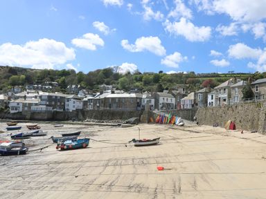 A beach with boats on sand and houses on a hill in the background at Lookout in Mousehole