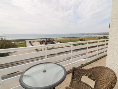 A balcony with a glass table and wicker chair overlooking a playground park and the sea at Sea Breeze in Marazion