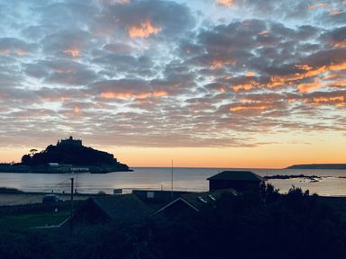 A coastal view at sunset with a castle on a hill and buildings near the shore at Sea Breeze in Marazion