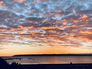 A sunset over a calm sea with scattered clouds and a silhouette of land and people at Sea Breeze in Marazion