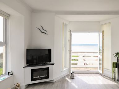 A living room with a wall-mounted tv and fireplace opens to a balcony with a sea view at Sea Breeze in Marazion