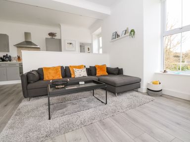A living room with a gray sectional sofa with orange and patterned cushions a black coffee table and gray rug at Sea Breeze in Marazion