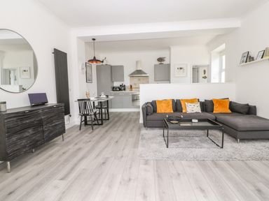 An open plan living room and kitchen with grey sofa and orange cushions at Sea Breeze in Marazion