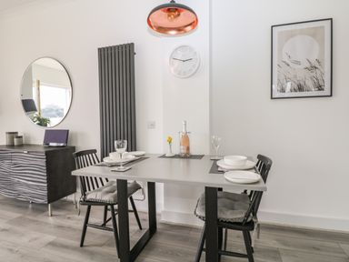 A dining area with a table set for four with chairs a sideboard with a round mirror a wall clock and framed artwork at Sea Breeze in Marazion