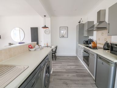 A kitchen with gray cabinets stainless steel appliances a white countertop and a small dining table at Sea Breeze in Marazion