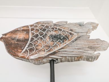 A carved wooden fish mounted on a black pole against a white wall at Sea Breeze in Marazion