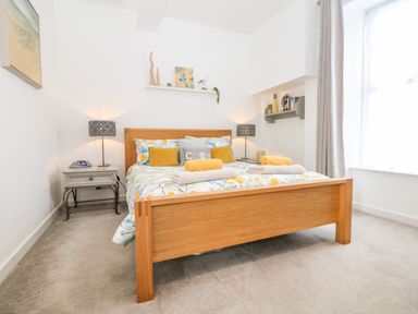 A bedroom with a wooden bed frame a floral duvet two bedside tables with lamps and a window with curtains at Sea Breeze in Marazion