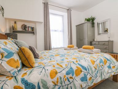 A bedroom with a bed with floral bedding and pillows a gray wardrobe a dresser with a mirror and plants at Sea Breeze in Marazion