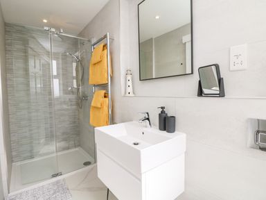 A bathroom with a glass shower enclosure white sink with black soap dispenser and cup yellow towels on a rack at Sea Breeze in Marazion