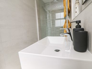 A bathroom sink with a faucet soap dispenser and cup with towels hanging in the background at Sea Breeze in Marazion