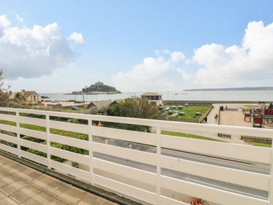 A balcony overlooking a road green area with boats playground and a sea with an island at Sea Breeze in Marazion