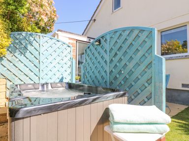 An outdoor hot tub next to blue lattice privacy screens with folded towels on a small table at Respryn Mevagissey