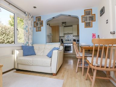 A living room with a white sofa with blue cushions a wooden dining table with chairs and a kitchen visible through an archway at Respryn Mevagissey