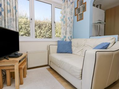 A small living room with a white leather sofa and blue cushions beside a window and a wooden side table with a television at Respryn Mevagissey