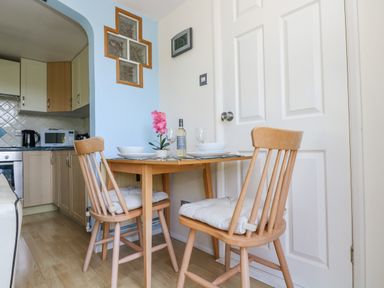 A small dining area with a wooden table and two chairs next to a kitchen and a white door at Respryn in Mevagissey