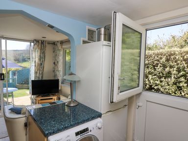 A kitchen area with a washing machine refrigerator and open door leading to garden at Respryn in Mevagissey