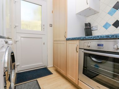 A kitchen with wooden cabinets a stainless steel oven a washing machine and a white door at Respryn in Mevagissey