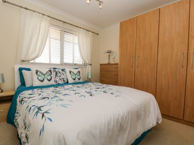 A bedroom with a double bed featuring butterfly cushions wooden wardrobe and chest of drawers at Respryn in Mevagissey