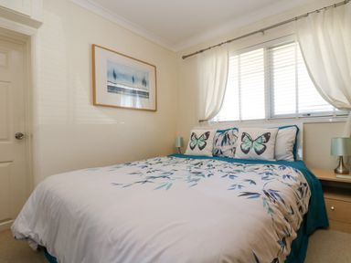A bedroom with a bed with butterfly pillows and floral bedding next to a window with white curtains at Respryn in Mevagissey