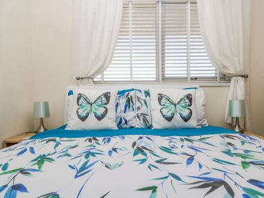 A bedroom with a bed covered in blue and green butterfly bedding and two nightstands with lamps at Respryn Mevagissey