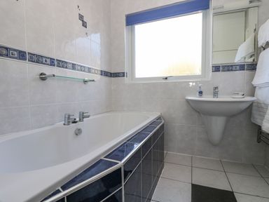 A bathroom with a bathtub a sink a window and tiled walls and floor at Respryn in Mevagissey