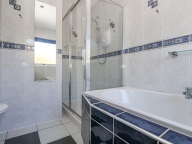 A bathroom with a bathtub shower enclosure a wall mirror and tiled walls at Respryn Mevagissey