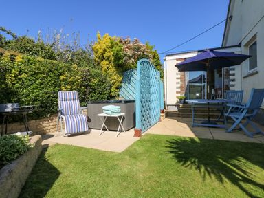 A garden patio with blue table and chairs under umbrella and reclining chair by a hot tub at Respryn in Mevagissey