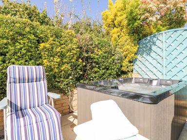 An outdoor hot tub with water jets next to a blue striped lounge chair and green bushes at Respryn in Mevagissey