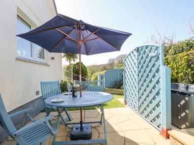 An outdoor patio with a blue table and chairs under a blue umbrella next to a lattice gate at Respryn in Mevagissey