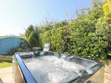 An outdoor hot tub with water jets and a chair next to a hedge and blue fence at Respryn Mevagissey