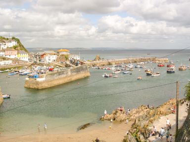 A coastal harbor with boats docked near a stone pier and people walking along a rocky shore at Respryn in Mevagissey
