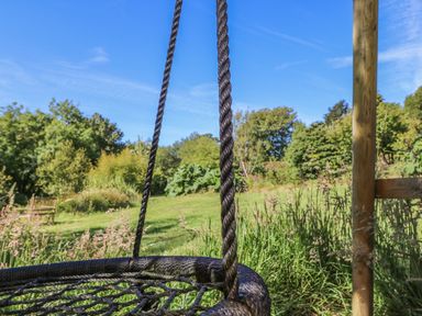 A close-up of a rope swing in a garden with grass trees and a wooden bench in the background at Pond Cottage in Stithians