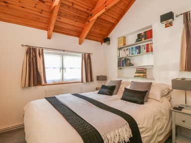 A bedroom with a double bed under wooden ceiling beams and a bookshelf at Pond Cottage in Stithians