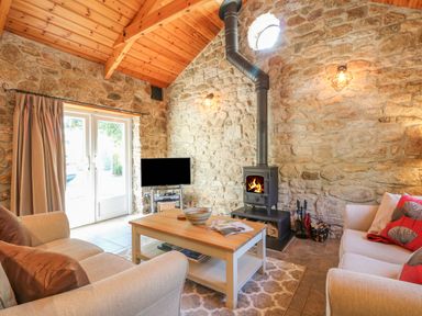 A living room with stone walls a wood burning stove a coffee table and two sofas at Pond Cottage in Stithians