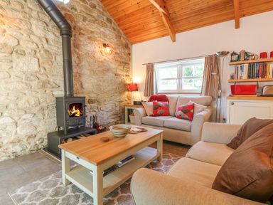A living room with a fireplace stone wall wooden ceiling two sofas a wooden coffee table and shelves at Pond Cottage in Stithians