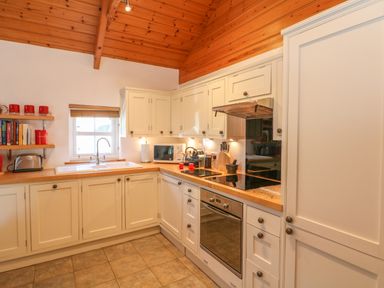 A kitchen with white cabinets a sink a stove an oven and shelves with books and red cups at Pond Cottage in Stithians