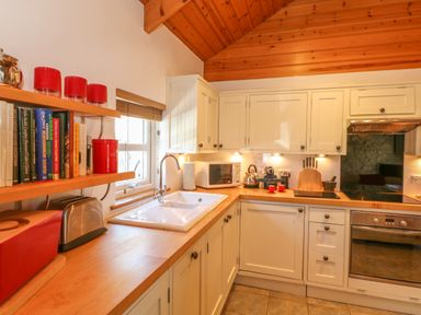 A kitchen with white cabinets wooden countertops shelves with books and containers and a window at Pond Cottage in Stithians