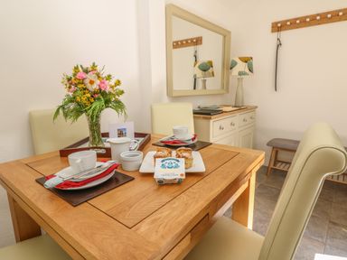 A dining area with a wooden table set for tea with cups scones and a vase of flowers at Pond Cottage in Stithians