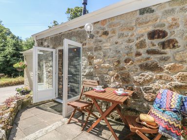 A small outdoor patio with a wooden table and chairs by a stone wall at Pond Cottage in Stithians