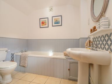 A bathroom with a toilet, bathtub, sink, framed pictures on the wall, and patterned tiles at Pond Cottage in Stithians
