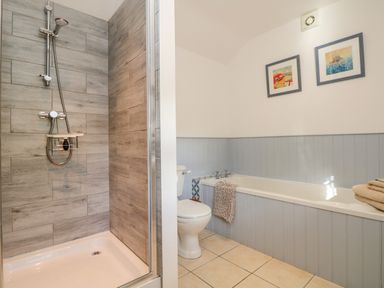 A bathroom with a shower, toilet, bathtub with towels, and two framed pictures on the wall at Pond Cottage in Stithians